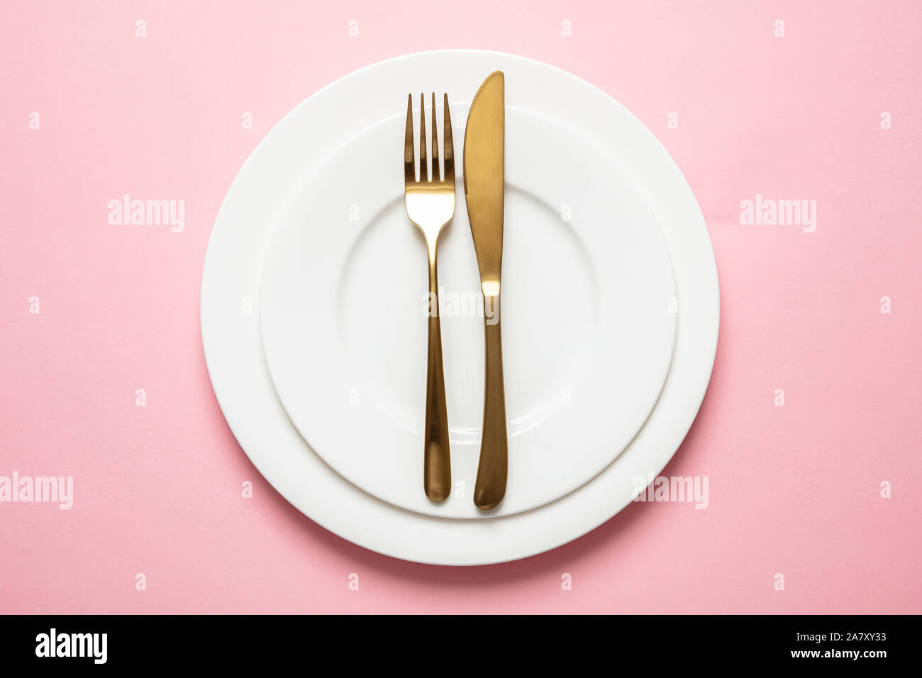 Oro e rosa lussuoso impostazione tabella. Golden set di posate e piatti bianchi contro sfondo rosa. Vista superiore, spazio di copia Foto Stock