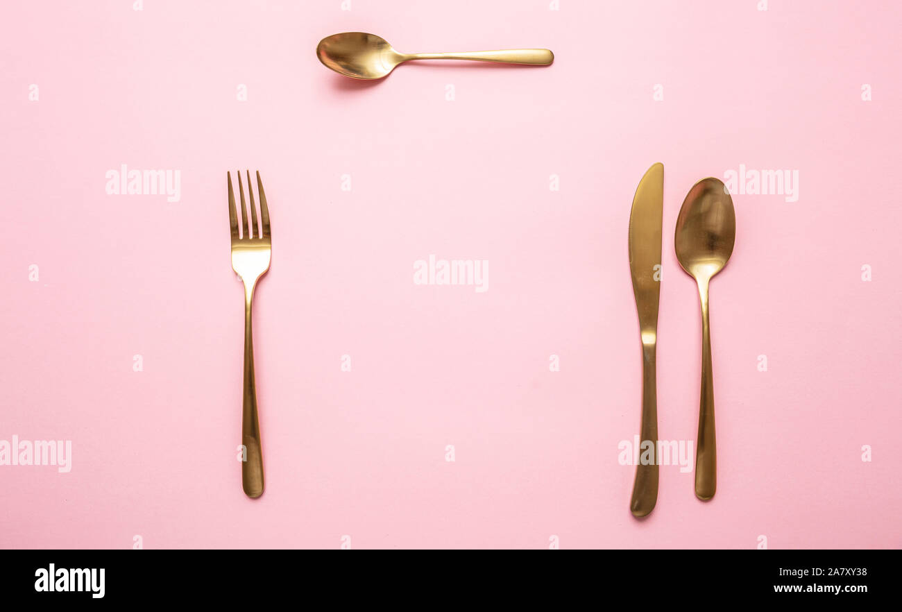 Oro e rosa lussuoso impostazione tabella. Golden set di posate contro sfondo rosa. Vista superiore, spazio di copia Foto Stock