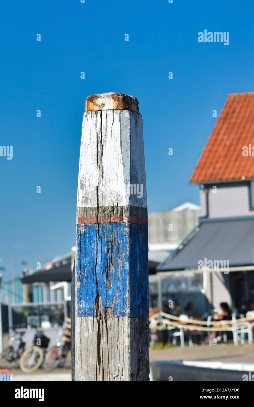 Palo di legno con il vecchio scaglie blu e vernice bianca per il fissaggio di imbarcazioni al porto di Oudeschild davanti a sfondo blu Foto Stock