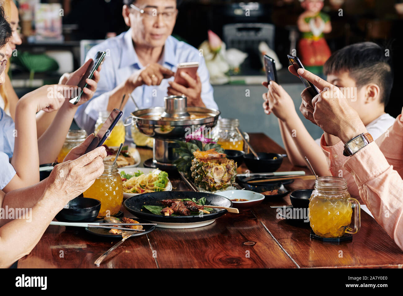 I membri della famiglia con gli smartphone di trascorrere del tempo sui social media invece di parlare durante la cena in famiglia Foto Stock