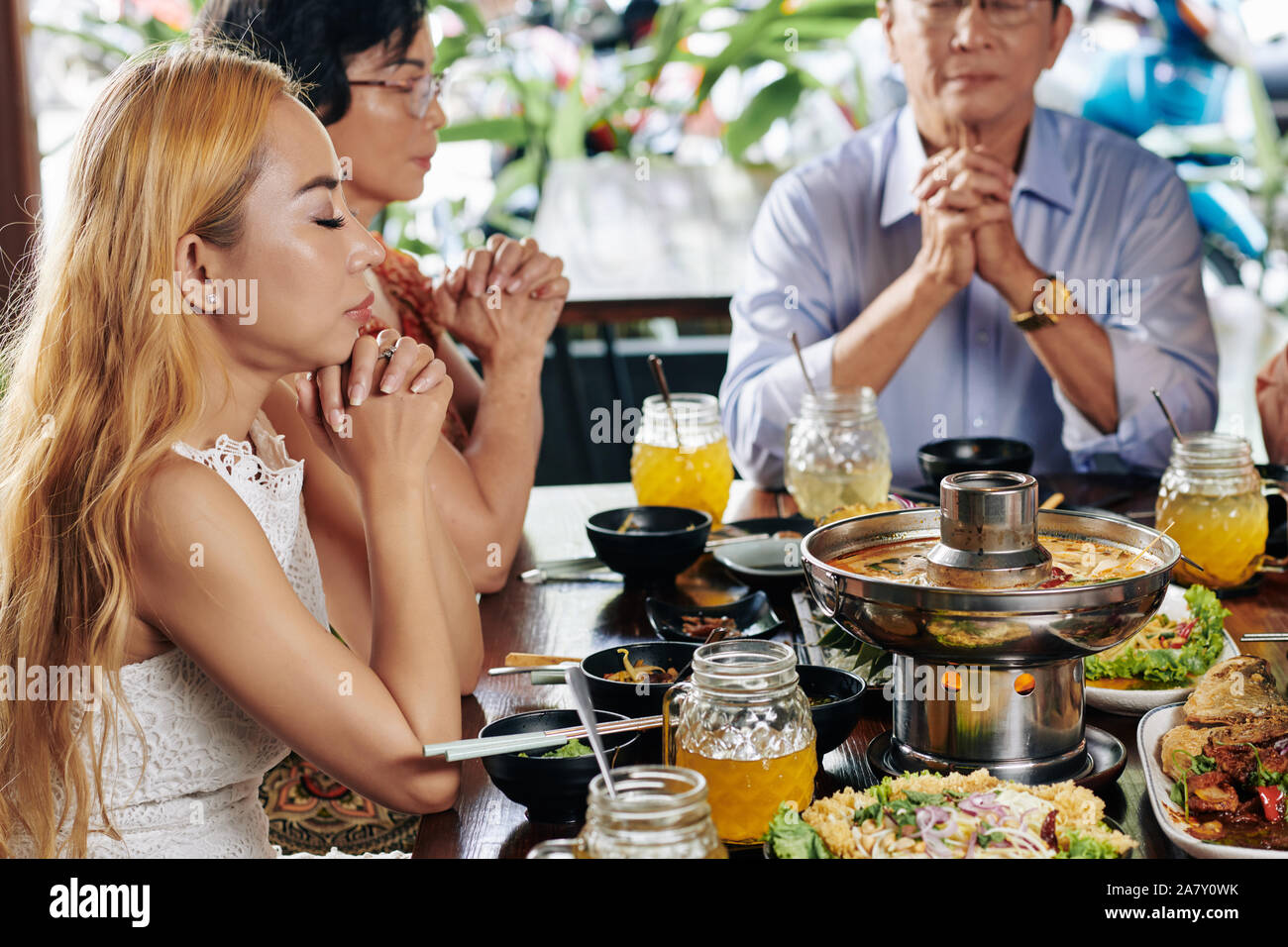 Giovane bella donna vietnamita di chiudere gli occhi e pregare con la sua famiglia prima di cena gustosa Foto Stock