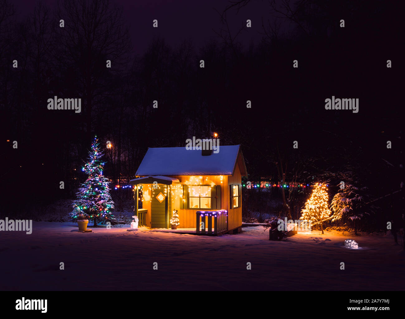 Carino, in legno dipinto di giallo private giochi per bambini casa nel giardino di casa, decorata con Natale LED luci di stringa all'aperto nel freddo nevoso nig avvolgitore Foto Stock