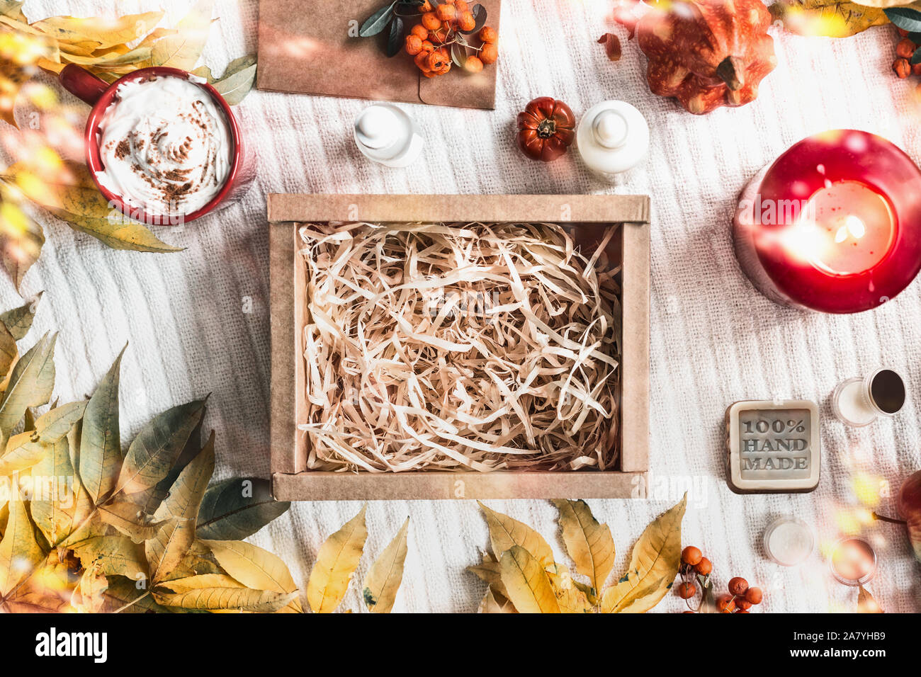 Svuotare la carta kraft box su coltre bianca con rami di autunno e cadono le foglie, tazza di cappuccino, prodotti cosmetici, candela che brucia e rowan. Era pari a zero Foto Stock