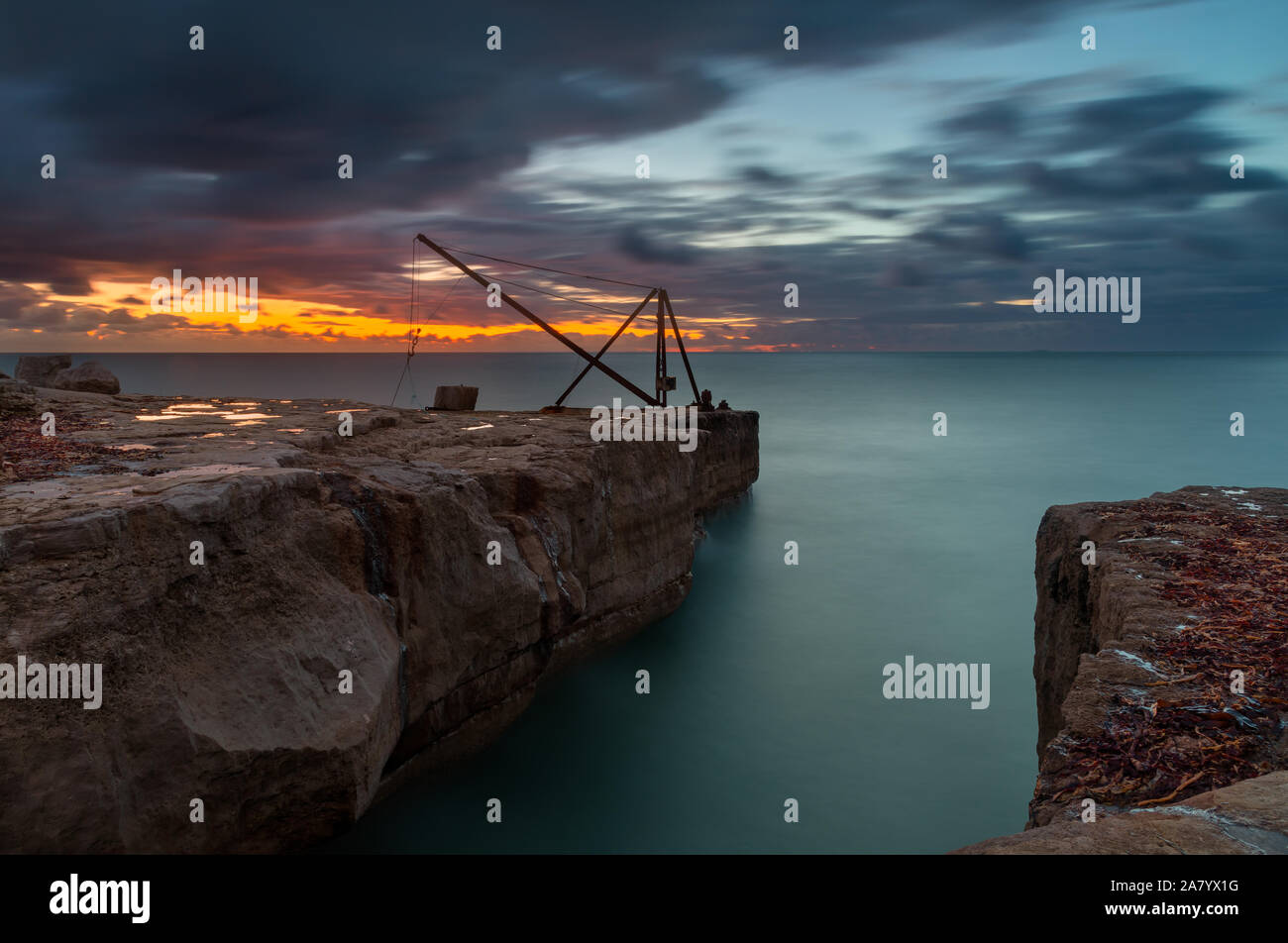 Portland Dorset Inghilterra Sunrise oltre la costa rocciosa a Portland Bill, parte del Dorset la Jurassic Coast, che mostra la vecchia barca Derrick, un ex c Foto Stock