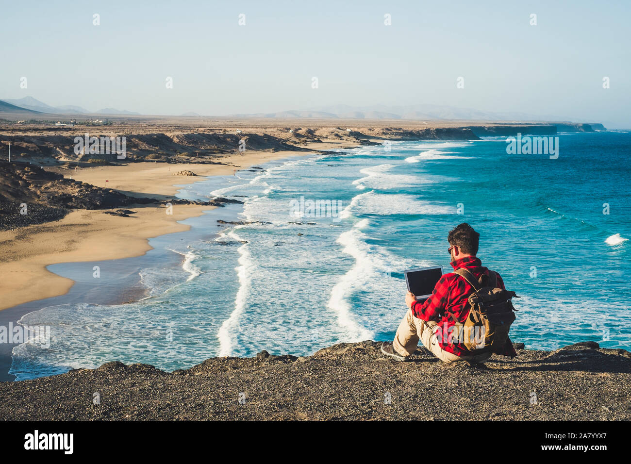 Il nomade digitale il concetto di stile di vita di uomo adulto sedersi sul terreno con vista panoramica della spiaggia e dell'oceano inbackground - lavorare con tecnologia internet Foto Stock