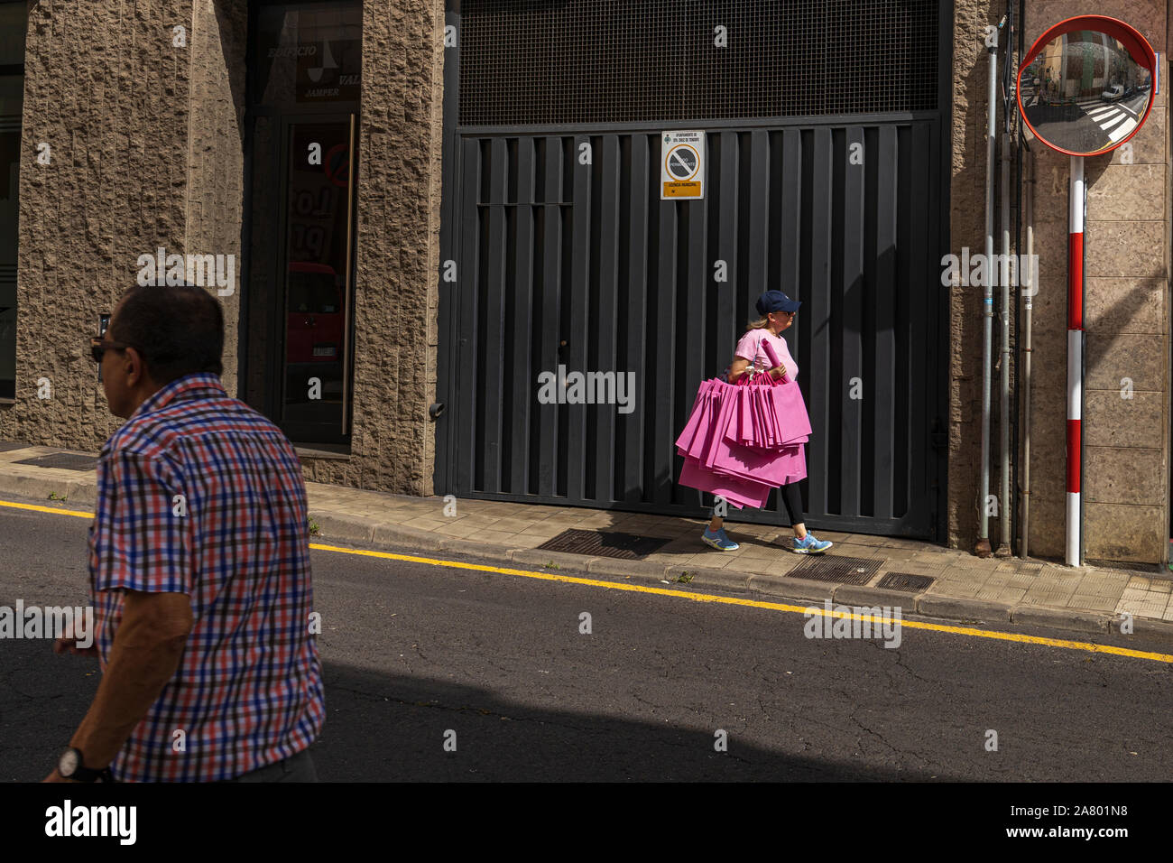 Donna con la bracciata di sacchetti rosa passeggiate da una porta di garage a Santa Cruz de Tenerife, Isole Canarie, Spagna Foto Stock