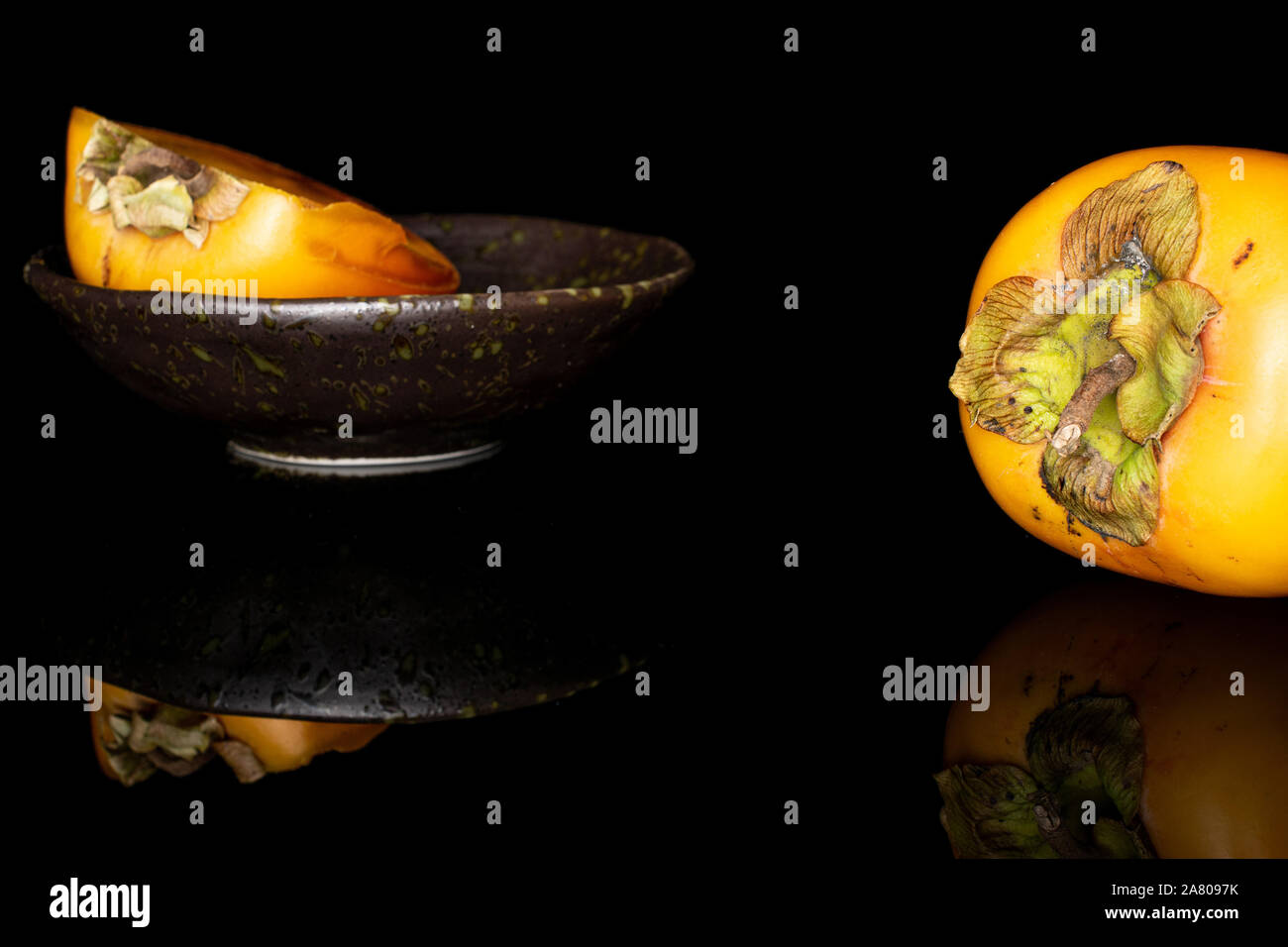 Gruppo di una intera metà di arancio dolce persimmon nel recipiente smaltato isolato sul vetro nero Foto Stock