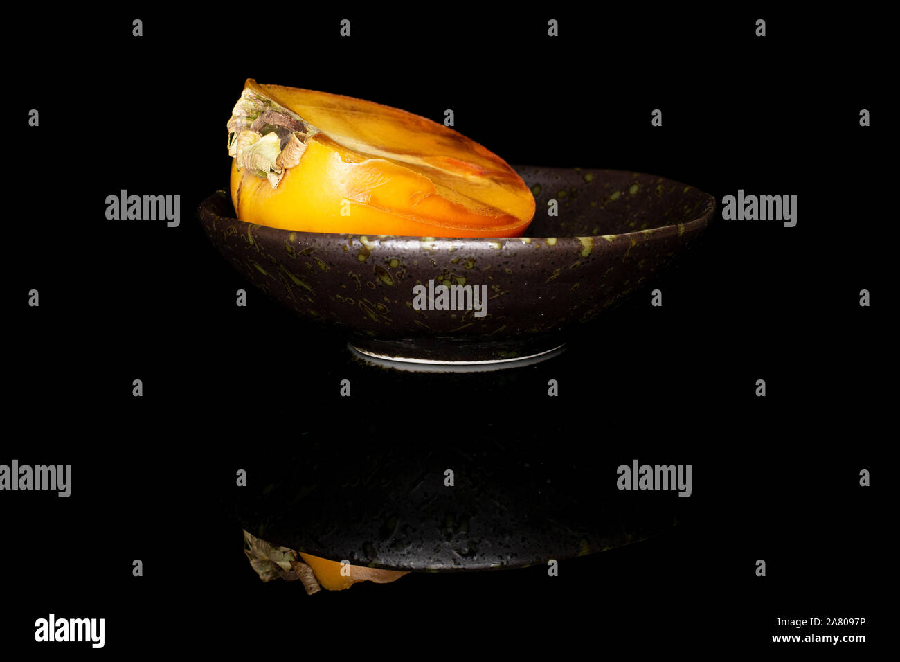 Una metà di arancio dolce persimmon nel recipiente smaltato isolato sul vetro nero Foto Stock