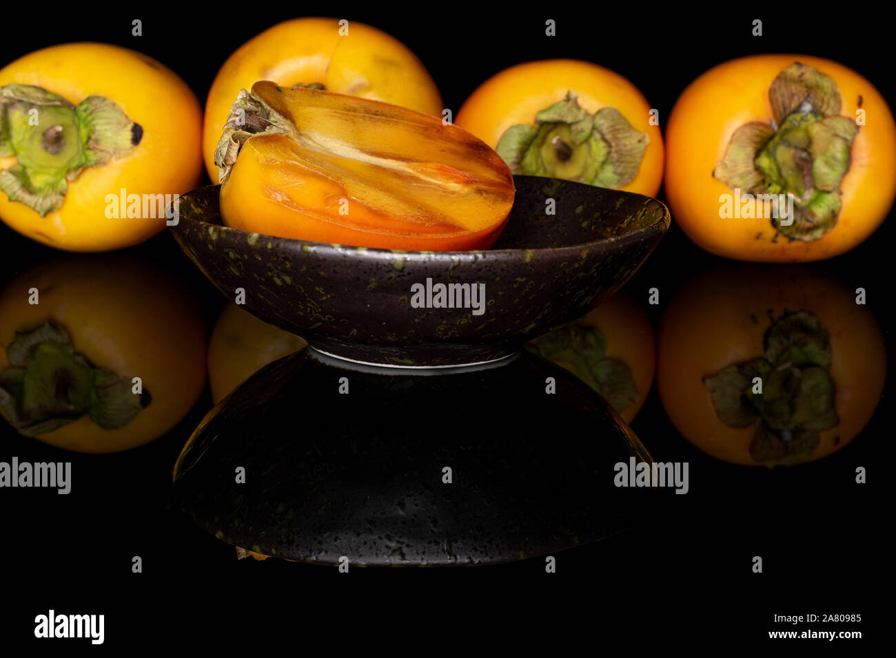 Il gruppo di quattro tutta una metà di arancio dolce persimmon nel recipiente smaltato isolato sul vetro nero Foto Stock