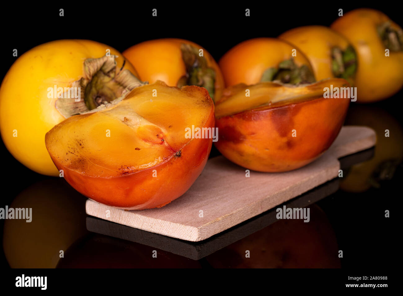 Il gruppo di cinque interi due metà di arancio dolce persimmon sul tagliere di legno isolata sul vetro nero Foto Stock