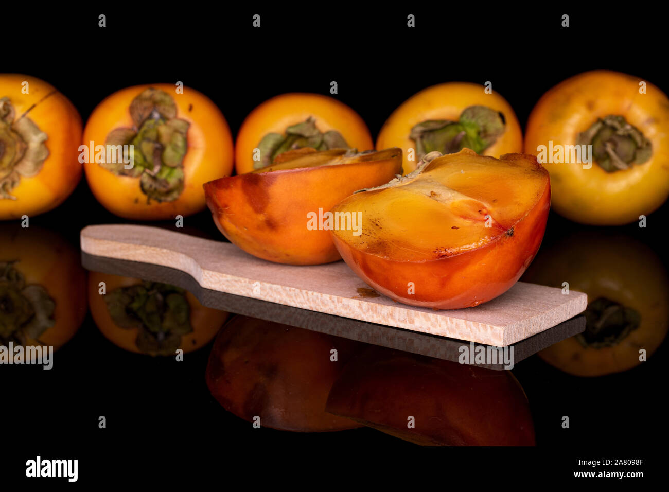 Il gruppo di cinque interi due metà di arancio dolce persimmon sul tagliere di legno isolata sul vetro nero Foto Stock