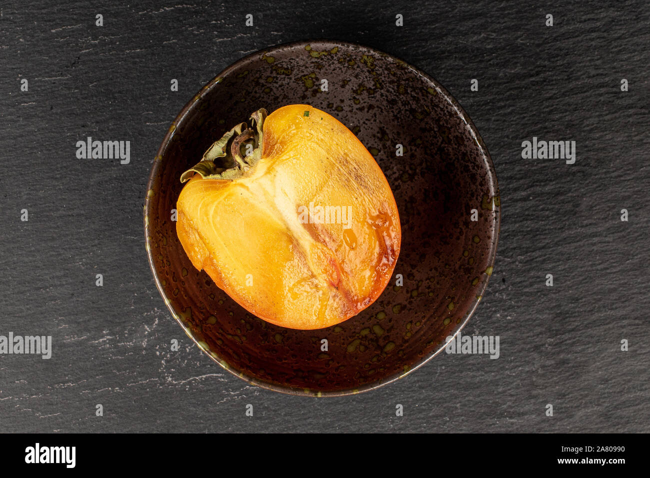 Una metà di arancio dolce persimmon nel recipiente smaltato flatlay sulla pietra grigia Foto Stock