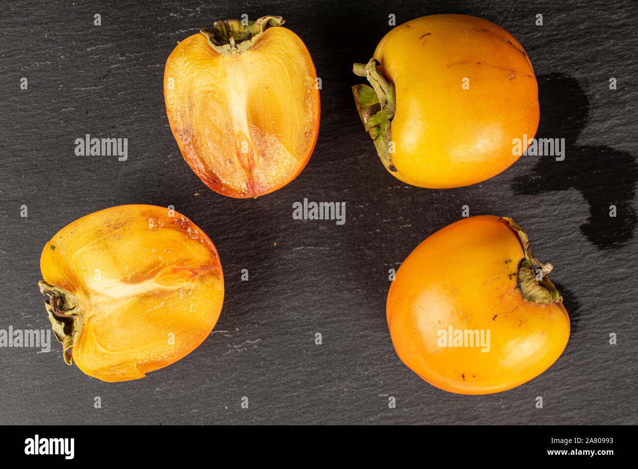 Gruppo di due interi due metà di arancio dolce persimmon flatlay sulla pietra grigia Foto Stock