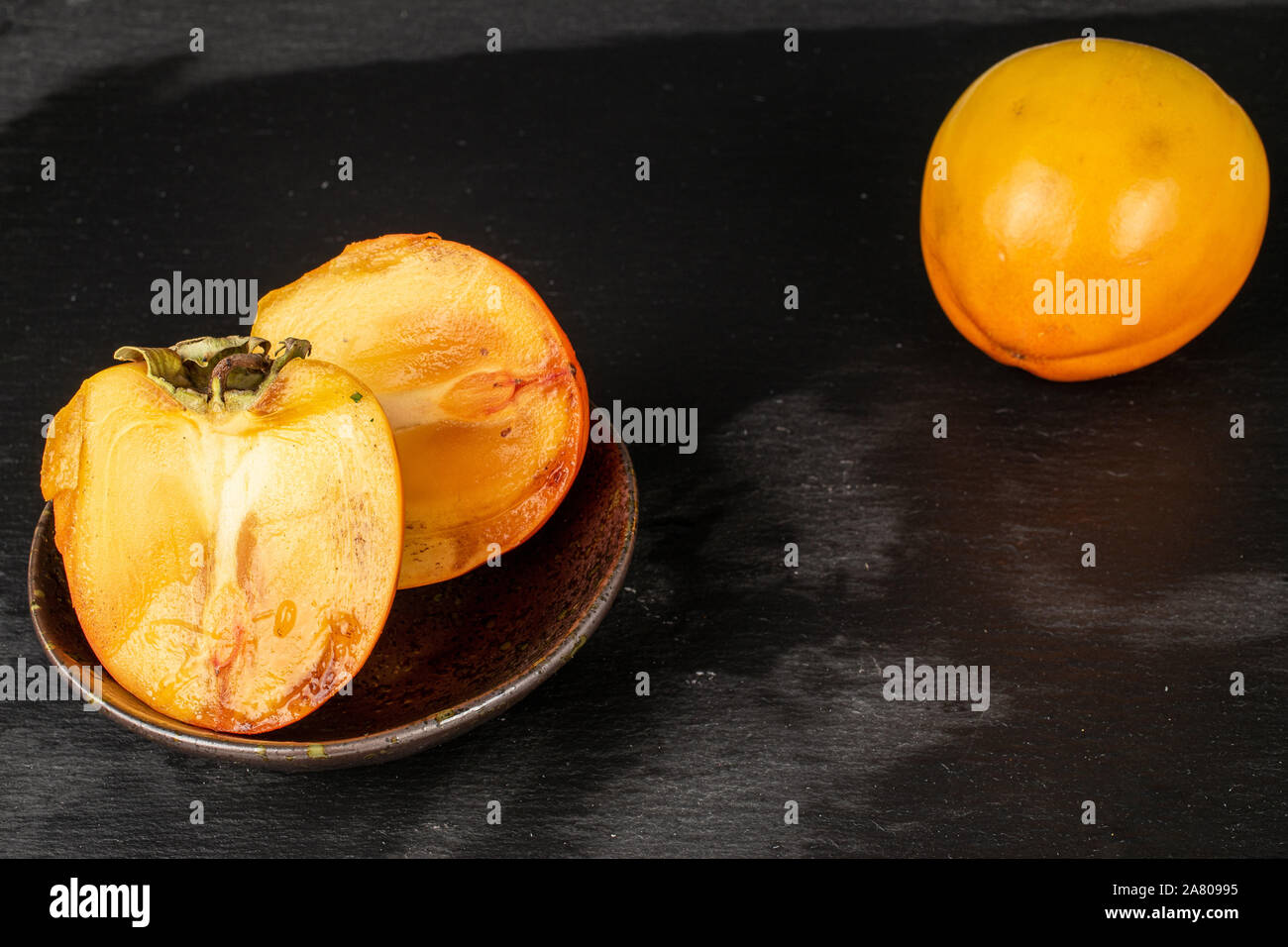 Gruppo di una intera due metà di arancio dolce persimmon nel recipiente smaltato sulla pietra grigia Foto Stock