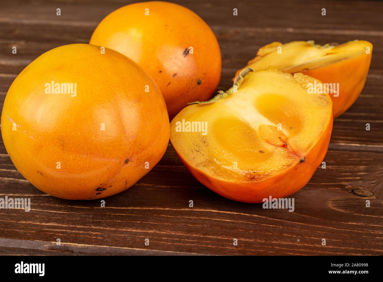Gruppo di due interi due metà di arancio dolce persimmon su legno marrone Foto Stock