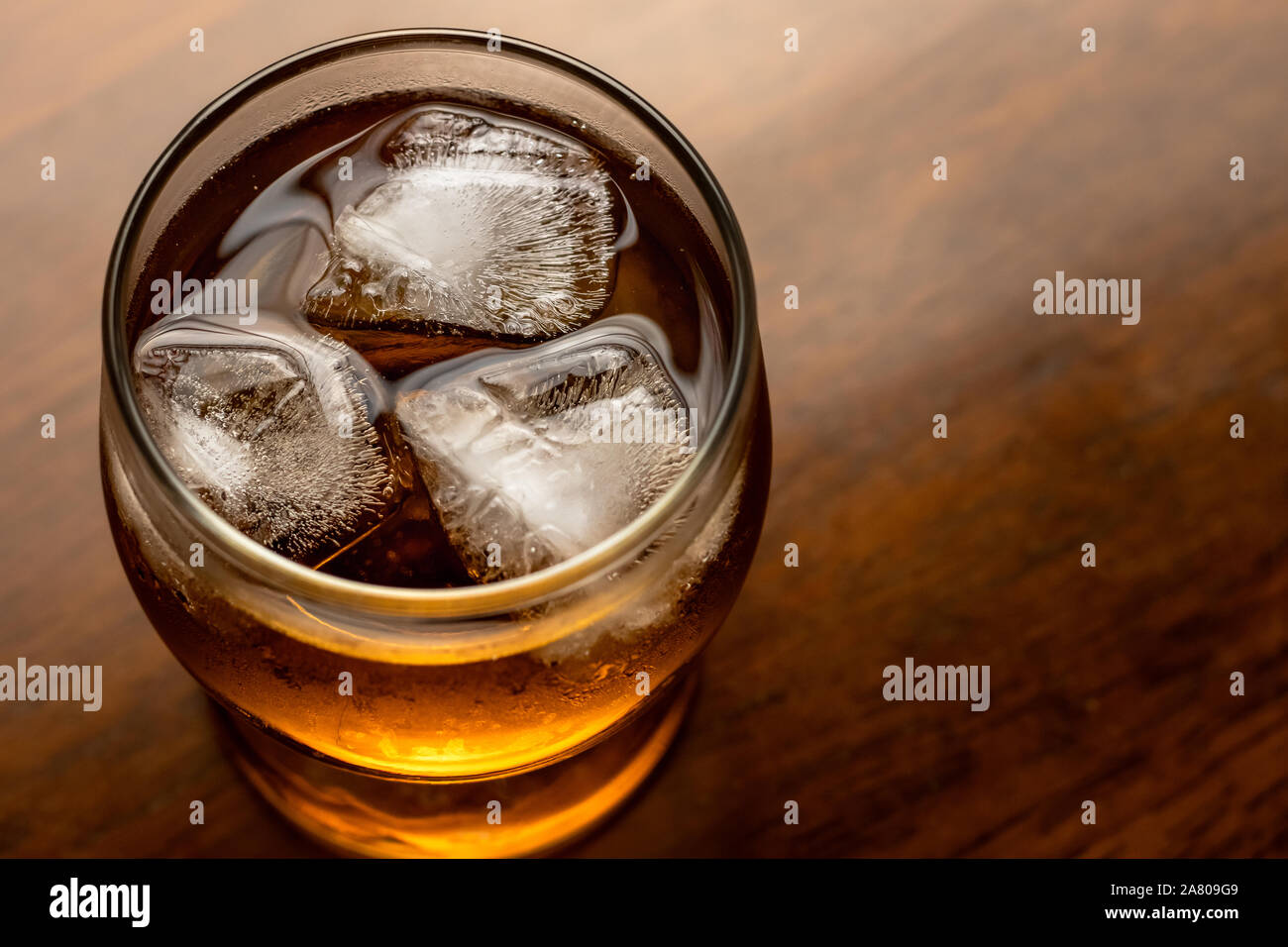 Bicchiere di whiskey con ghiaccio su sfondo di legno. Borbone su legno scuro tavolo. Alcol bevanda marrone con bolle. Raffreddato il rum, vista dall'alto di close-up. Testo spac Foto Stock