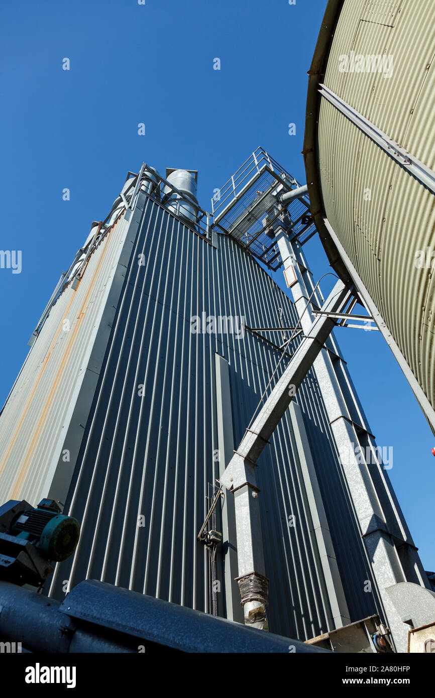 Guardando oltre un verde silos, towartds industriale essiccatore di grano con un cielo blu sullo sfondo Foto Stock