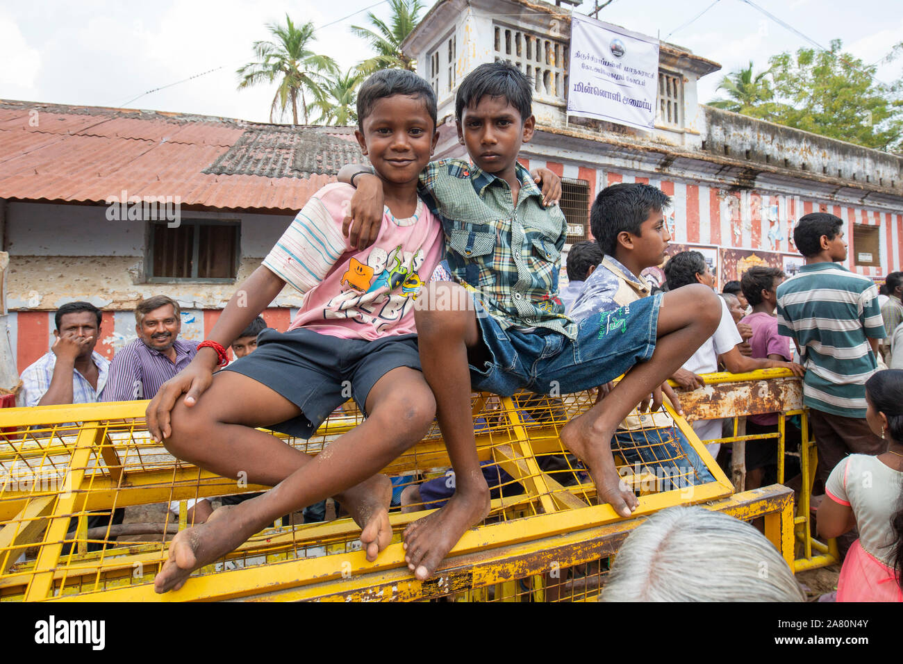 Due giovani ragazzi seduti su un recinto giallo guardando il Kutti Kudithal Festival di Trichy, Tamil Nadu, India Foto Stock