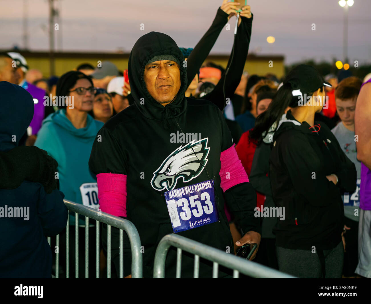 Uomo ispanico in felpa con cappuccio e altri concorrenti attendono la mattina presto inizio del 2019 Porto Mezza Maratona nel Corpus Christi, Texas USA. Foto Stock