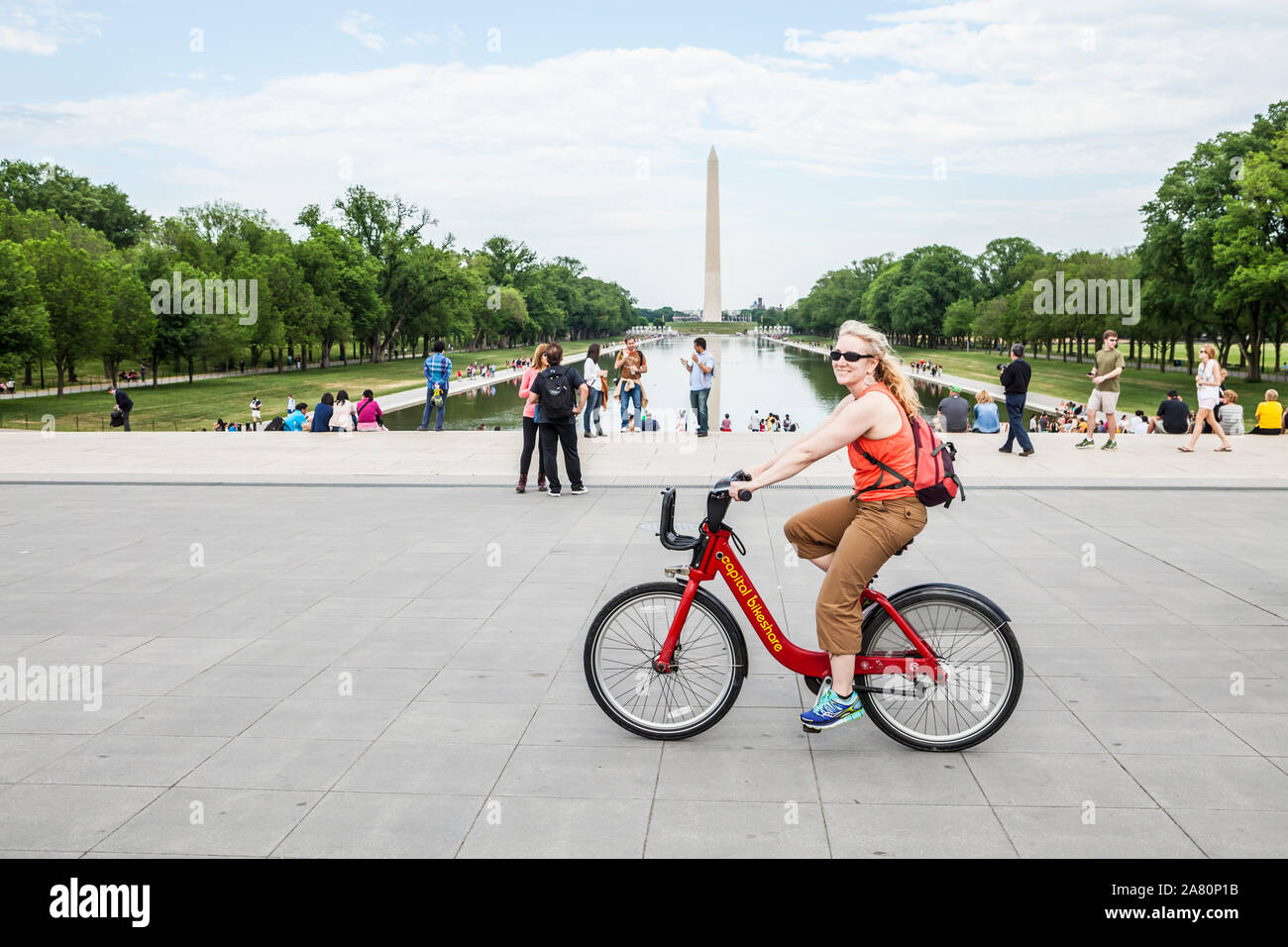 Una donna felice in sella a una moto condividi bike sul National Mall di Washington D.C., USA. Il Monumento di Washington in background. Foto Stock