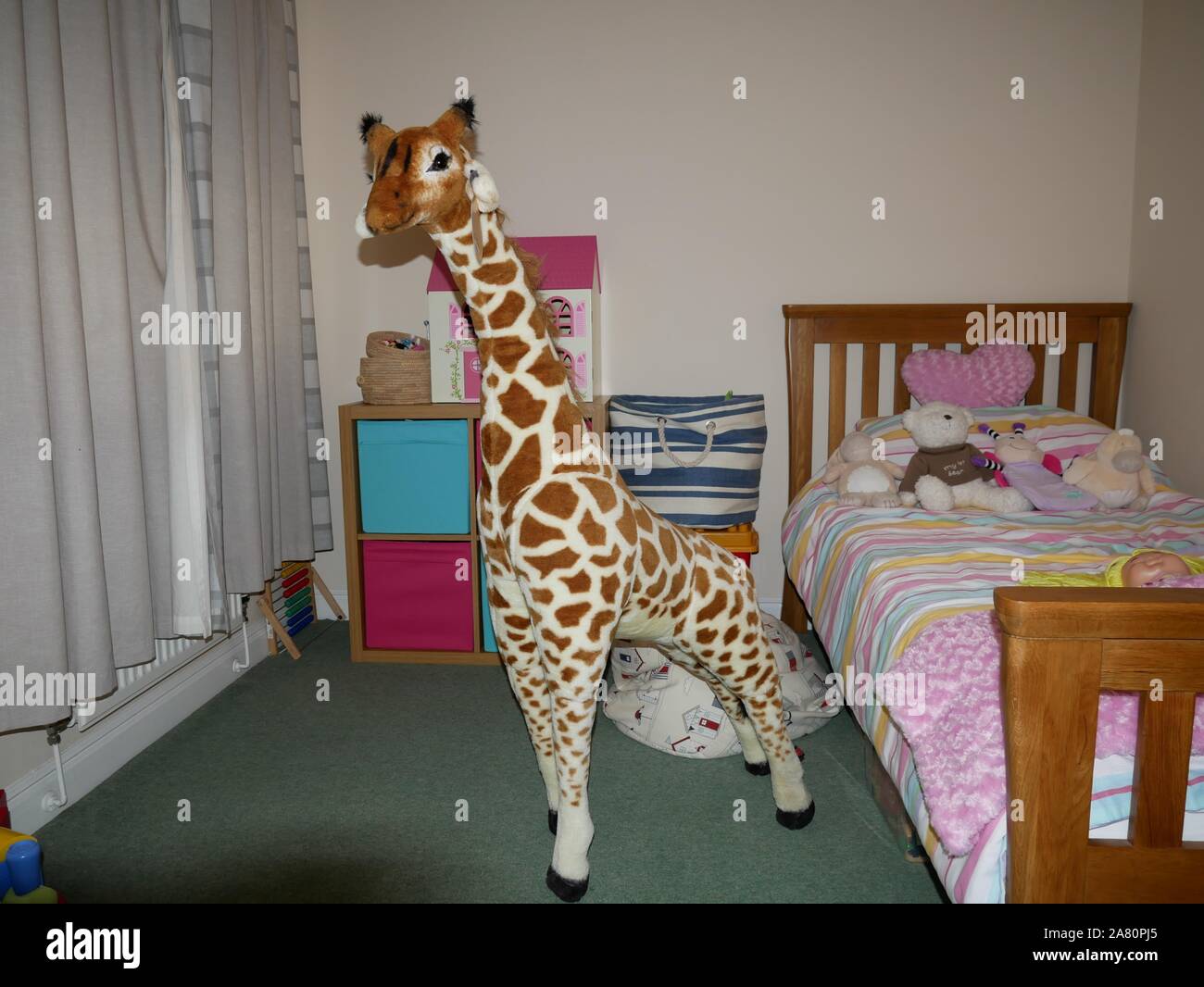 Una grande e di colore marrone e bianco toy giraffa e altri giocattoli in una camera da letto per i bambini Foto Stock