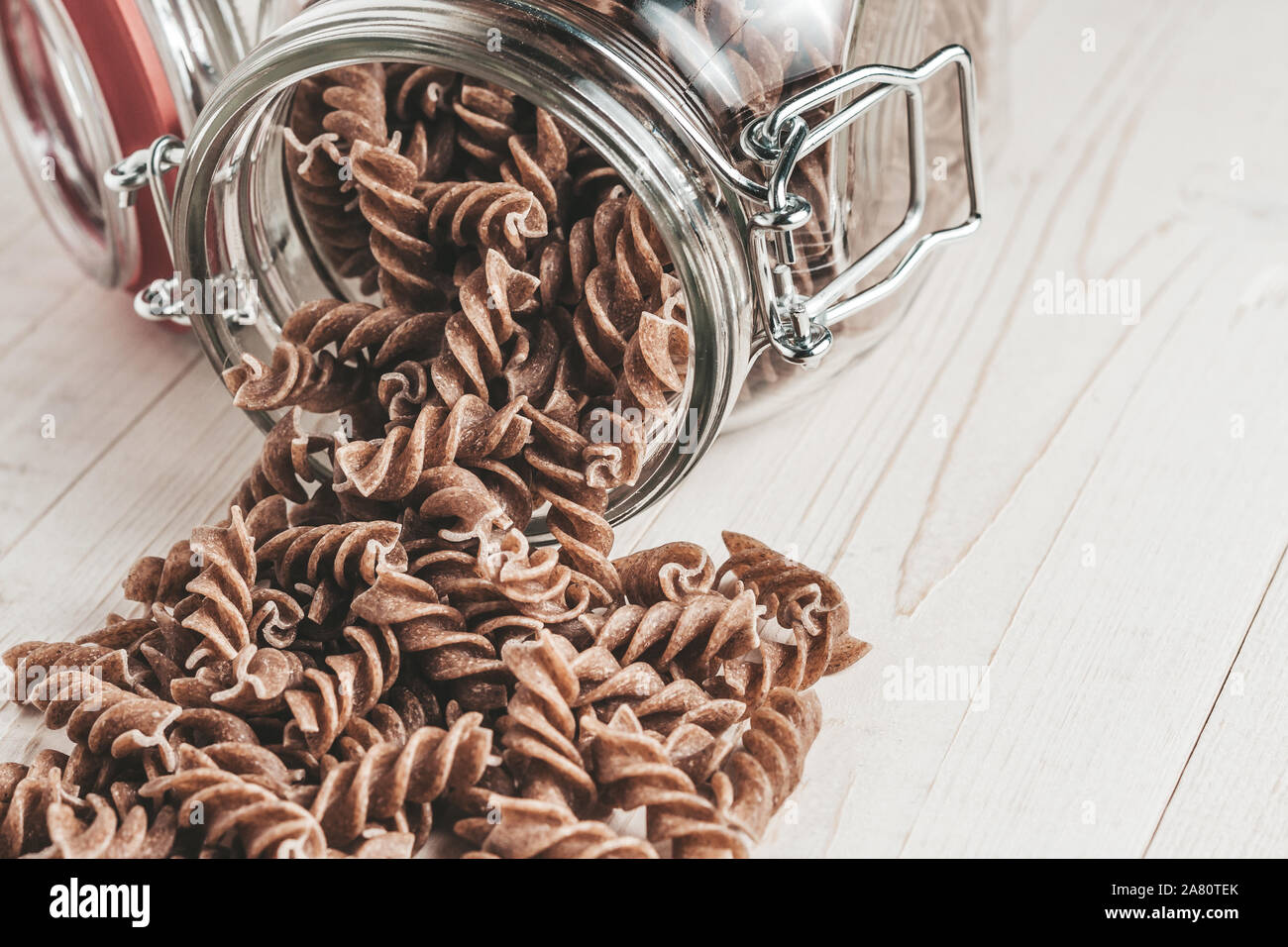 Maccheroni fusilli versata da un aperto il vasetto di vetro su un bianco tavolo in legno Foto Stock