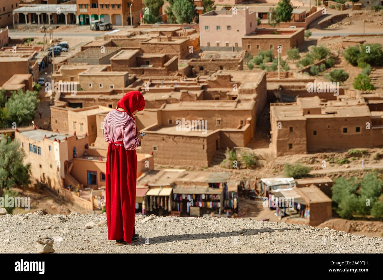 La donna araba vestita in rosso sembra presso la Mobil nella Kasbah Ait Ben Haddou in Ouarzazate, Marocco Ottobre 2019 Foto Stock