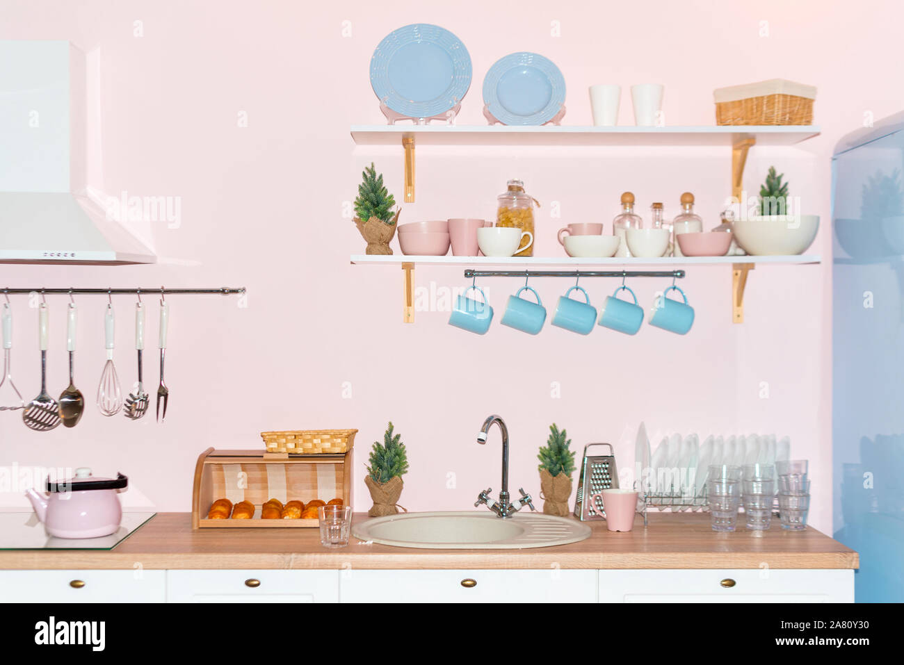 Rosa e blu pastello cucina moderna interni. Accessori da cucina, contenitori con cereali, piatti e appendere tazze blu. Foto Stock