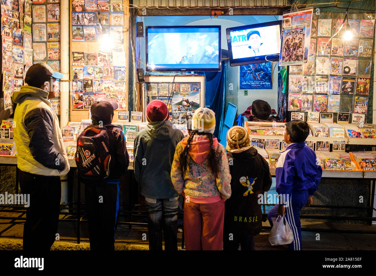 Gruppo di bambini a guardare un film su un negozio che vende la copia illegale di film in DVD per le strade di Copacabana di notte, Bolivia Foto Stock