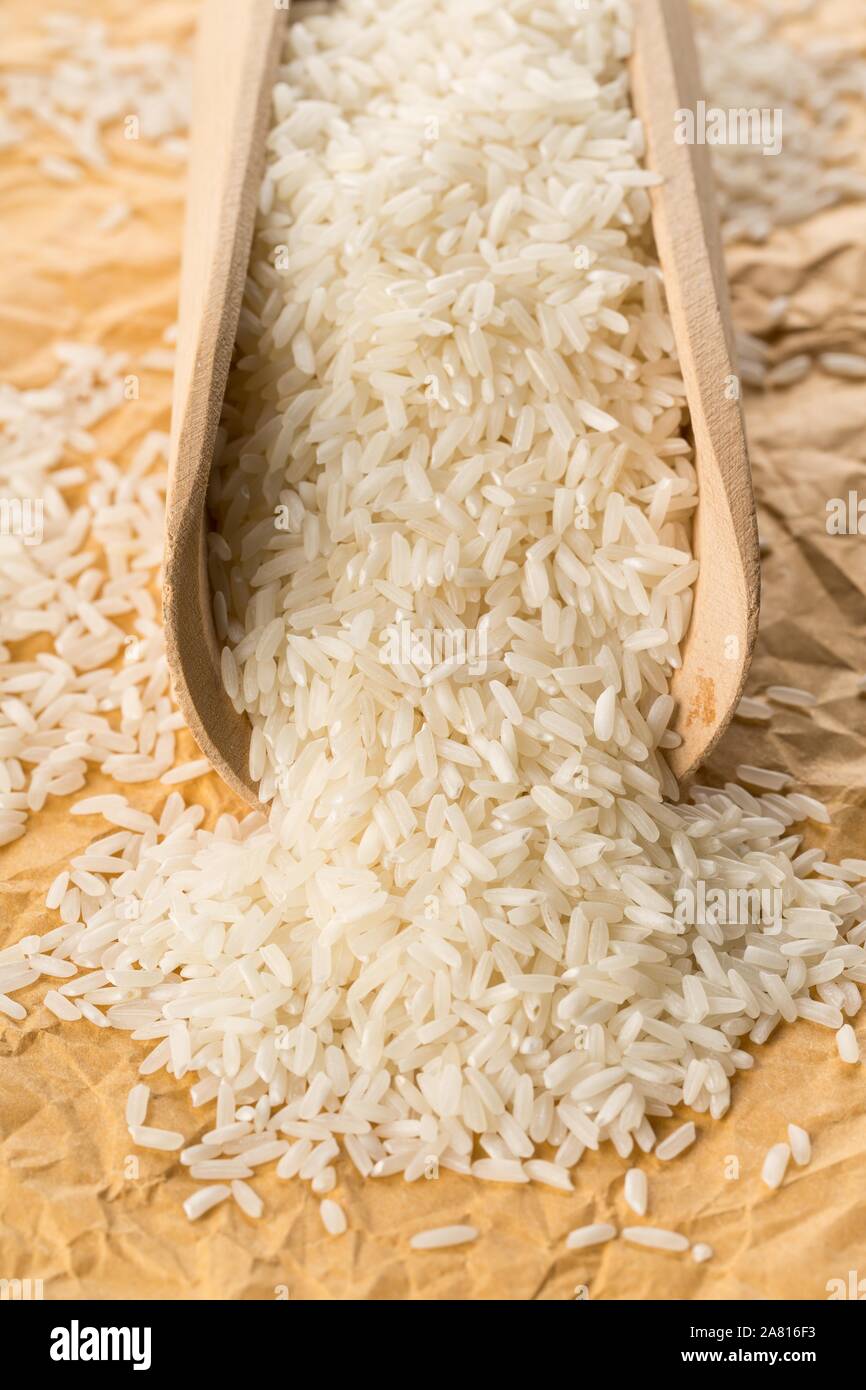 Mucchio di bianco non cotti, crudi riso a grani lunghi in legno da scoop su marrone carta da imballo sullo sfondo - Il fuoco selettivo Foto Stock