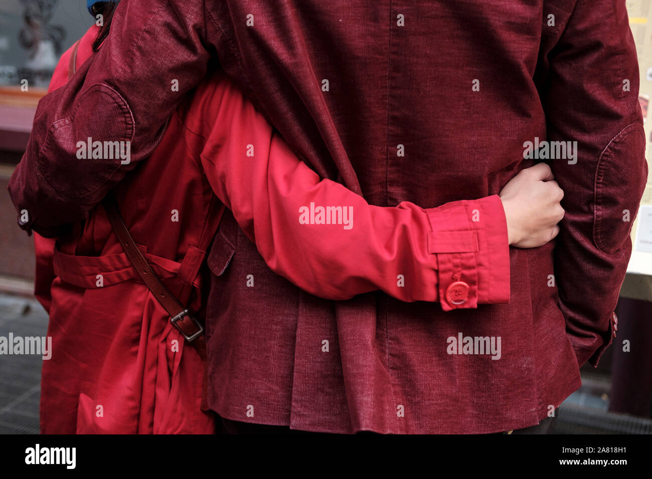 Giovane indossando matching cappotti rossi abbracciare ogni altro- vista posteriore, London, Regno Unito Foto Stock