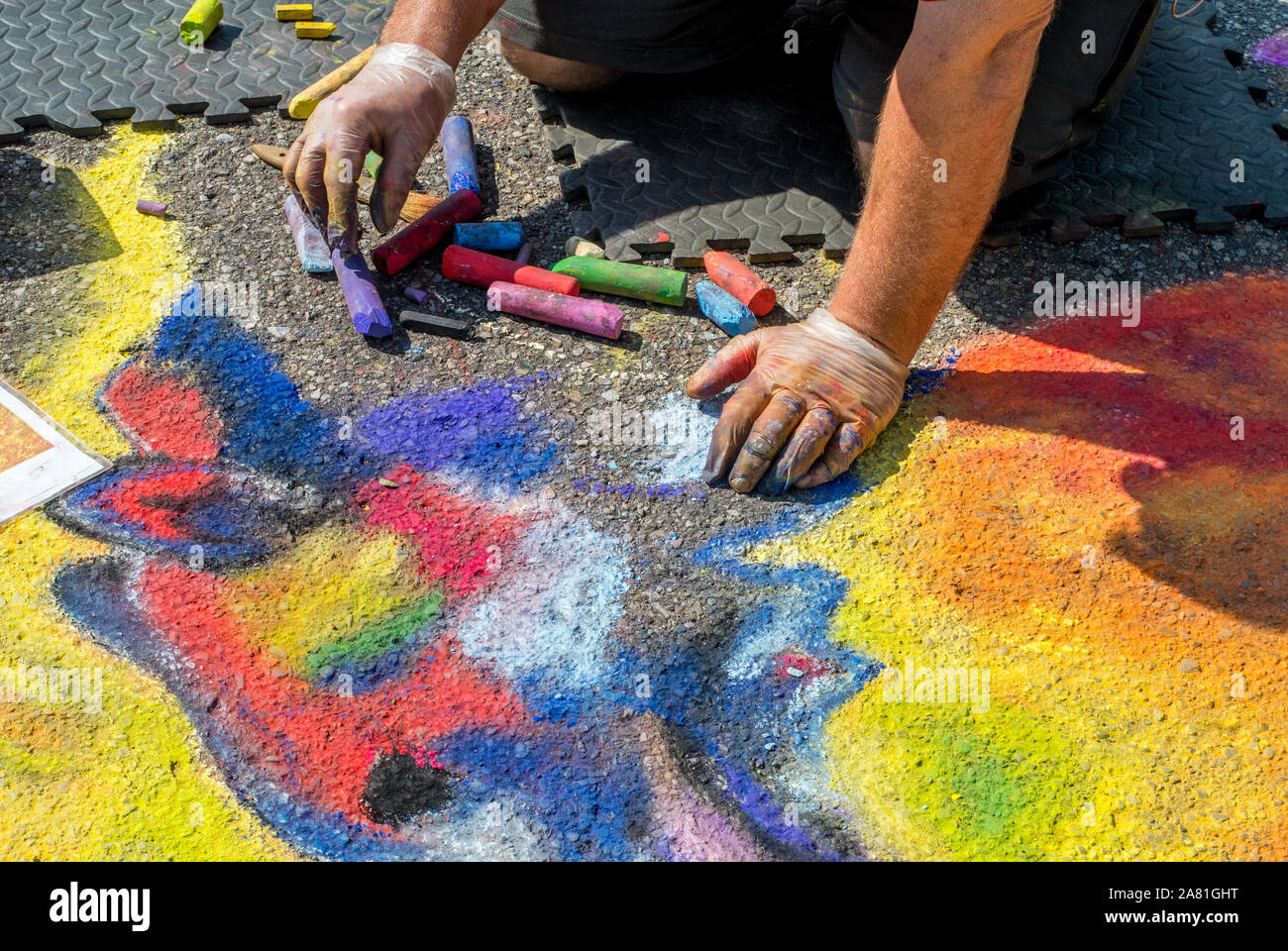 Un'artista utilizza Chalk e pastelli per creare arte temporanea su un asfalto street Foto Stock