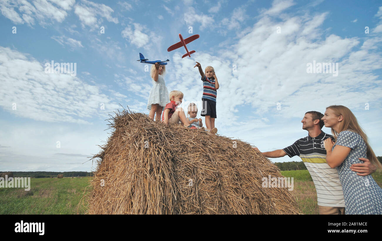 Bambini lanciare aeroplani mentre in piedi su una pila di paglia davanti ai loro genitori. Foto Stock