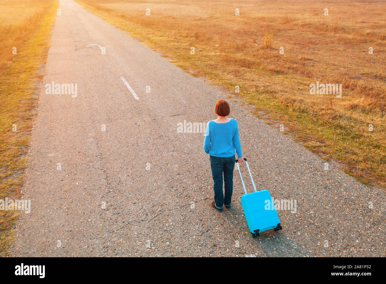 Tirando la donna valigia viaggio bagagli su strada in autunno tramonto, elevato angolo vista da fuco pov Foto Stock