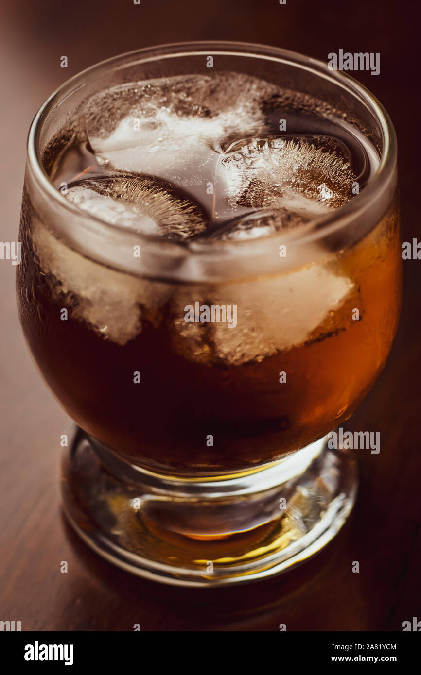 Bicchiere di whiskey con ghiaccio sul legno scuro dello sfondo. Bevande alcoliche. Un singolo oggetto. Macro shot. Foto Stock