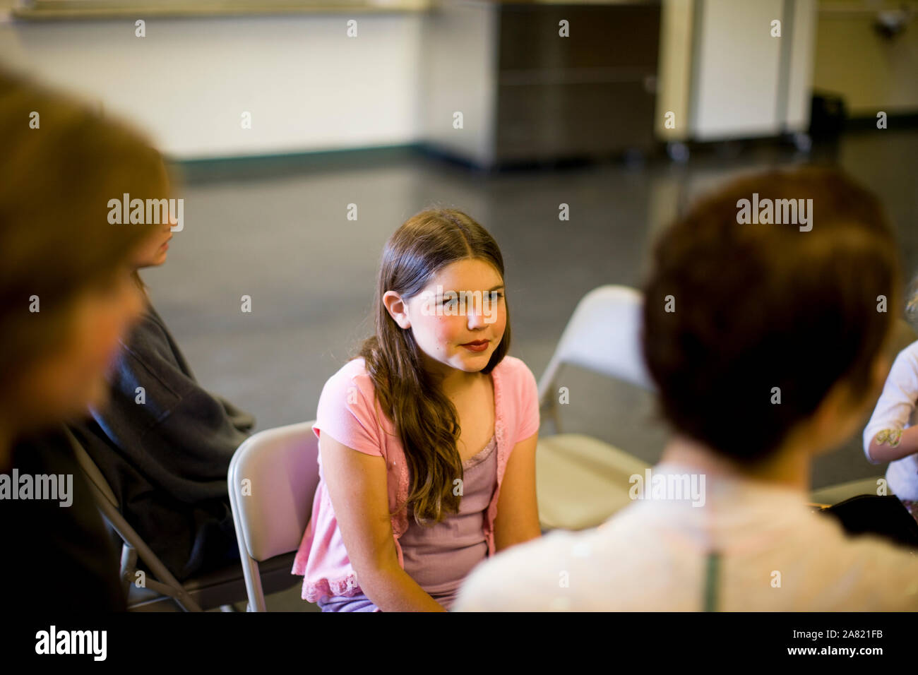Ragazza seduta su una sedia tra gruppo di persone Foto Stock