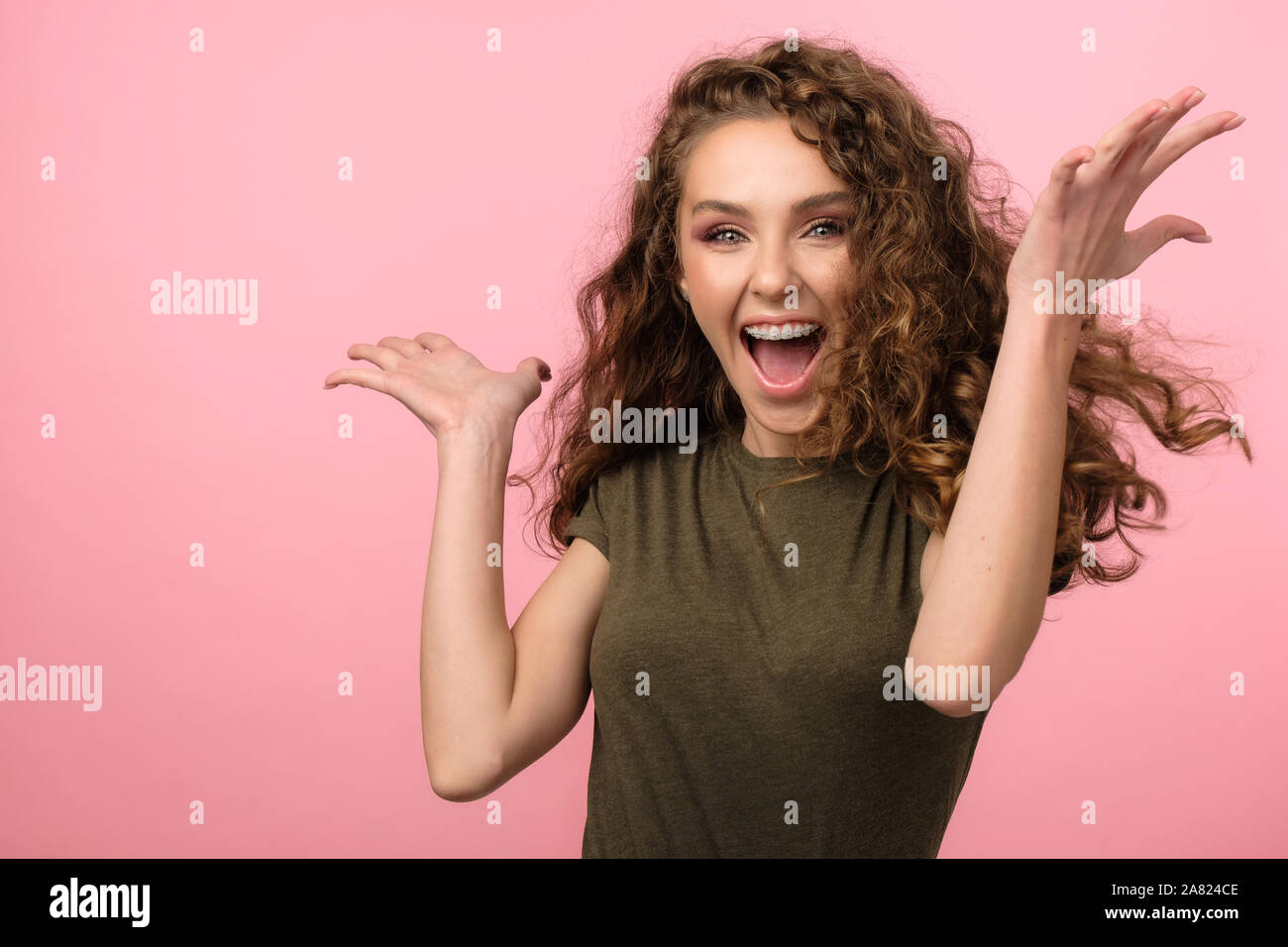 Attraente ragazza con i capelli ricci esprimere emozioni isolato su sfondo rosa Foto Stock