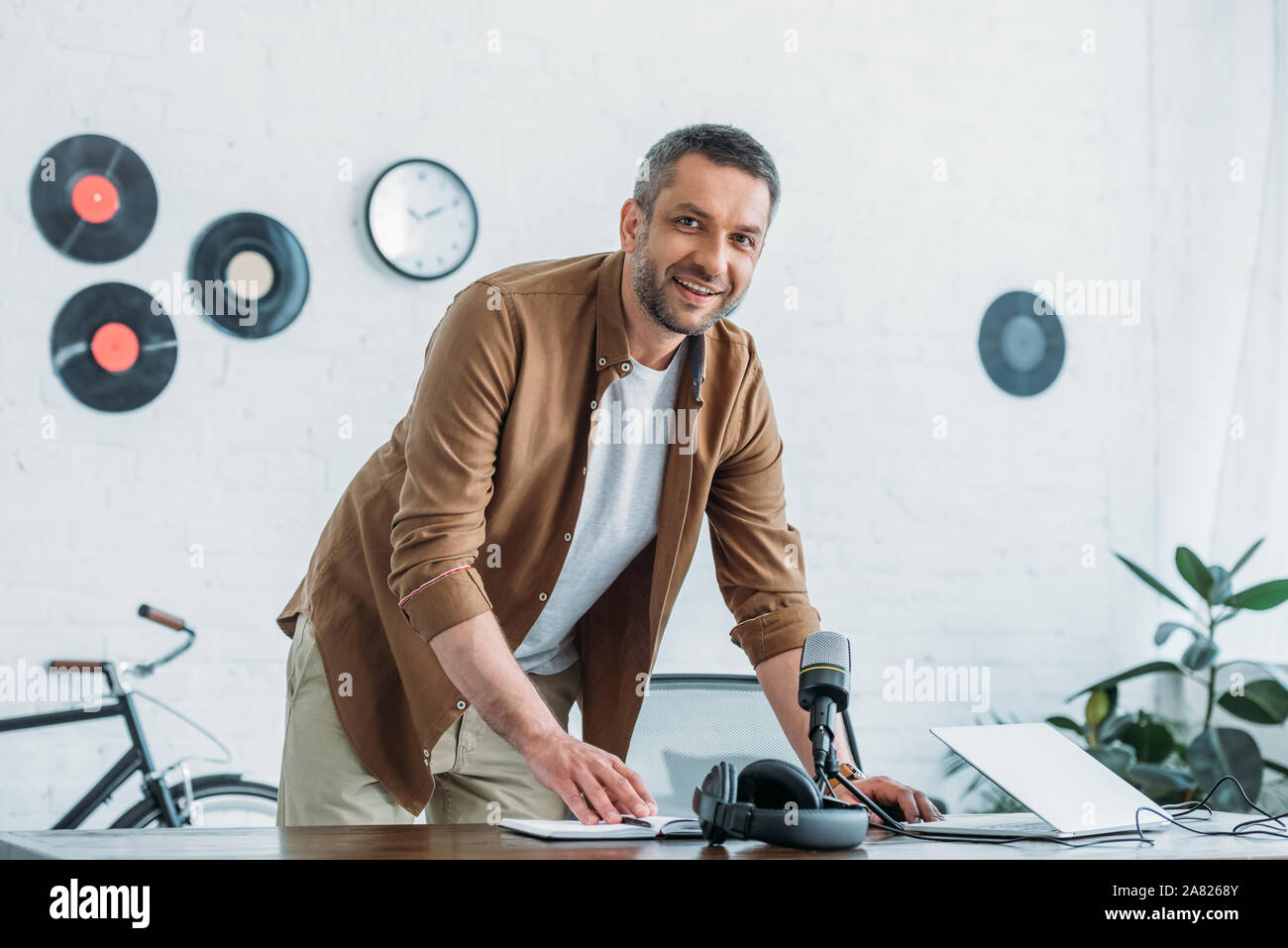 Bello host radio sorridente alla videocamera mentre si sta in piedi in luoghi di lavoro in studio di trasmissione Foto Stock
