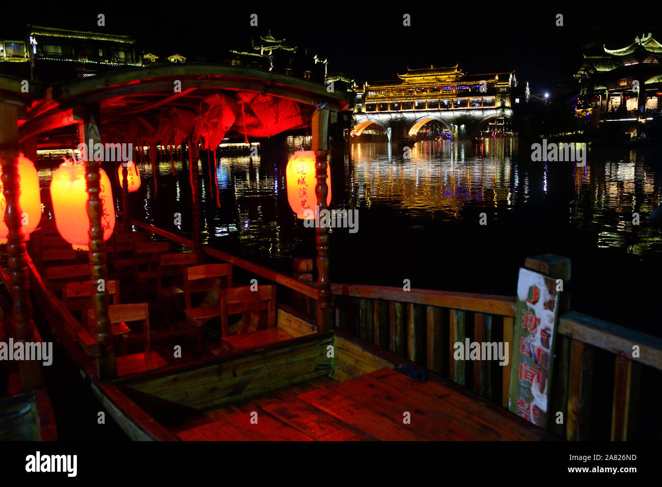 Un inserito tour in barca si siede in attesa per i turisti per imbarcarsi sul tuo Jiang River a galleggiare sotto il Phoenix Hong ponte di Fenghuang Città Antica, un favo Foto Stock