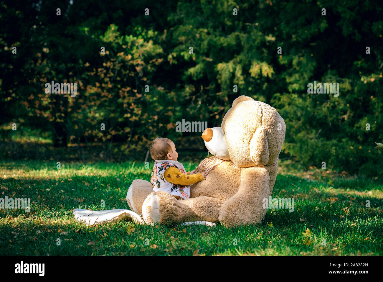 Poco carino bambino sta giocando con un big bear su un prato verde. Foto Stock