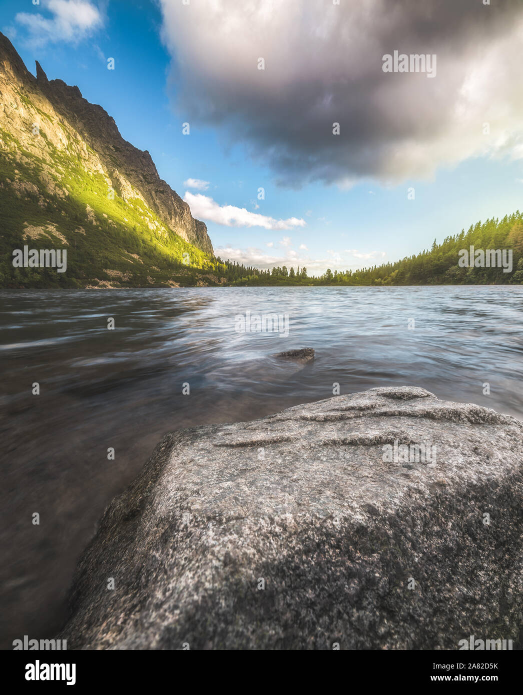 Lago di montagna con la roccia in primo piano e parzialmente illuminata Hill. Poprad Tarn, Alti Tatra, Slovacchia. Foto Stock