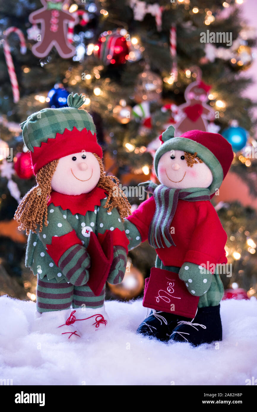 Una simpatica coppia di Natale bambole caroler posano con il loro canto di libri, di fronte all'albero di Natale Foto Stock