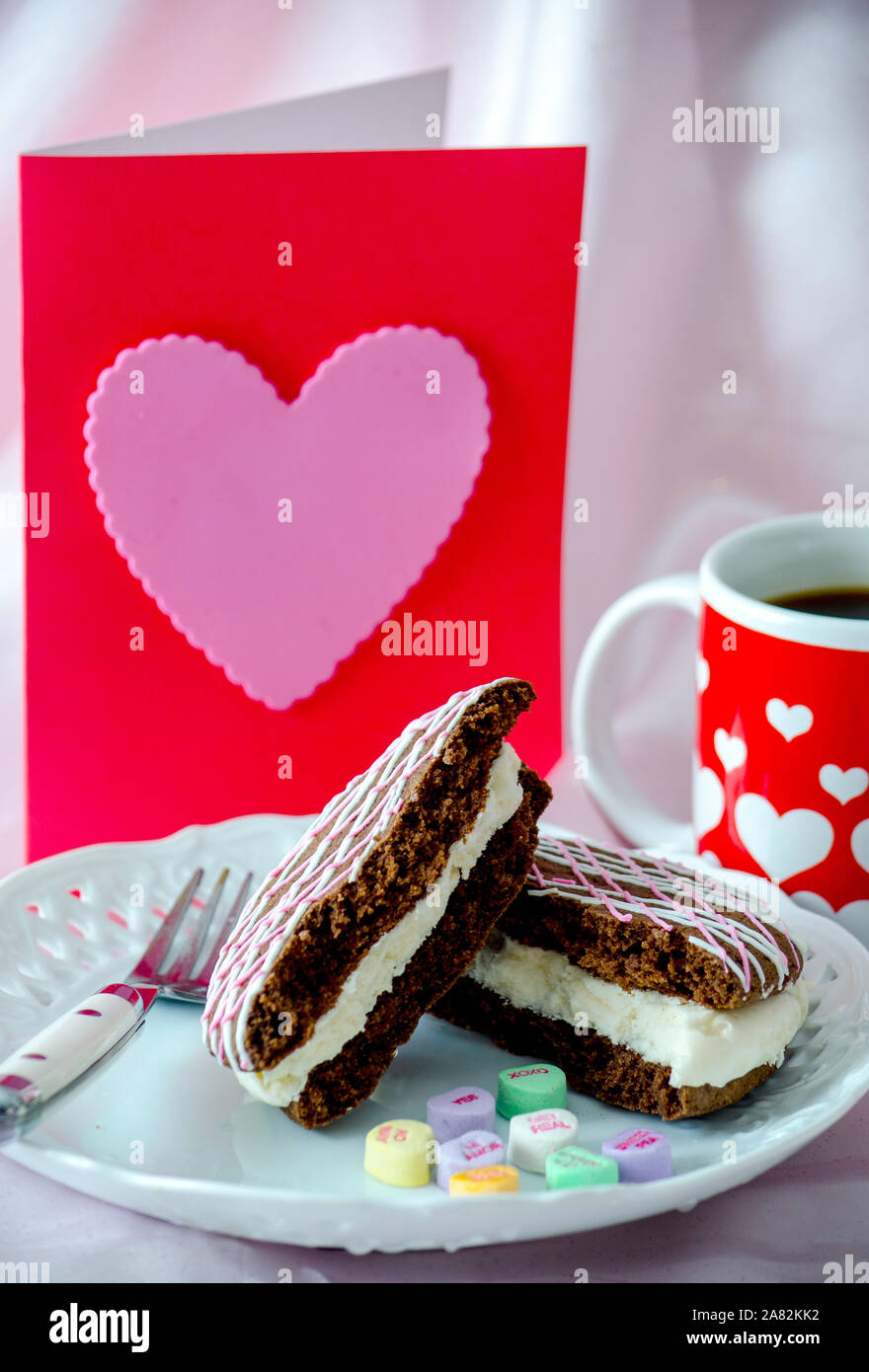 Un cuore buono regalo e un cuore decorato la tazza di caffè lungo con una torta al cioccolato torta di whoopee caramella e cuori Foto Stock