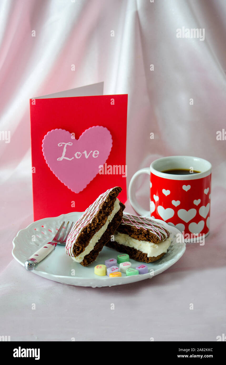 Un cuore decorato la tazza di caffè lungo con una torta al cioccolato torta di whoopee e cuore rosa card Foto Stock
