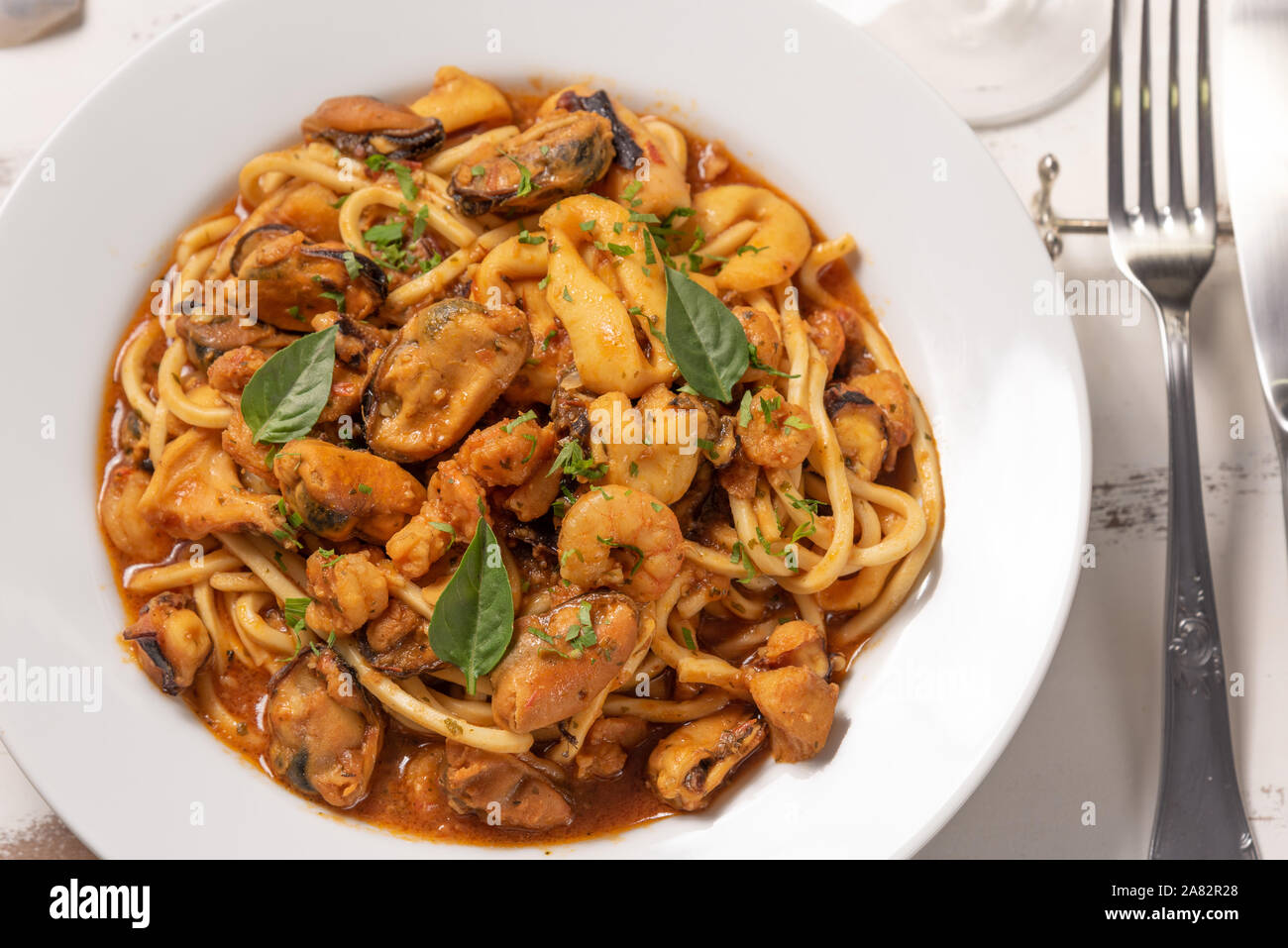 Pasta con frutti di mare in piastra bianca su un bianco sullo sfondo di legno, luce morbida. Spaghetti ai frutti di mare, specialità di pesce e frutti di mare gastronomia mediterranea Foto Stock