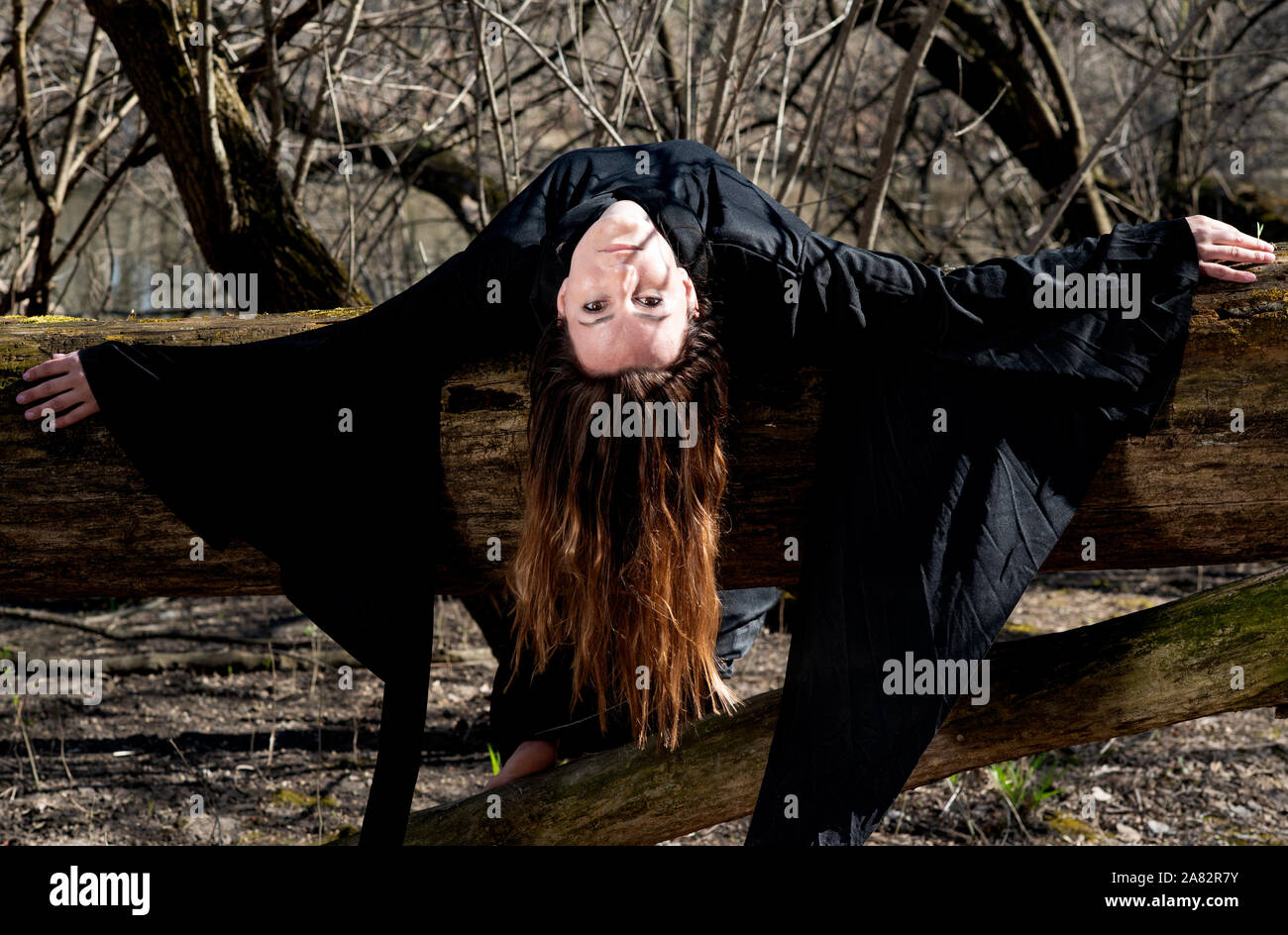 Donna con scuri capelli lunghi in black robes appesi sui rami di alberi in mezzo alla foresta. Torna al concetto di natura. Strega. La stregoneria e magia. Foto Stock