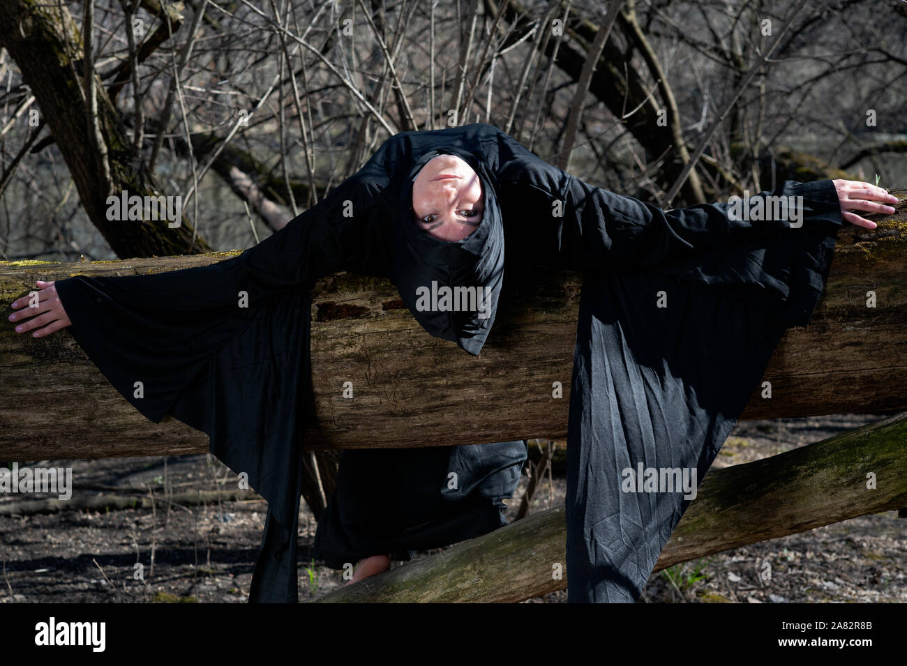 Donna con scuri capelli lunghi in black robes appesi sui rami di alberi in mezzo alla foresta. Torna al concetto di natura. Strega. La stregoneria e magia. Foto Stock