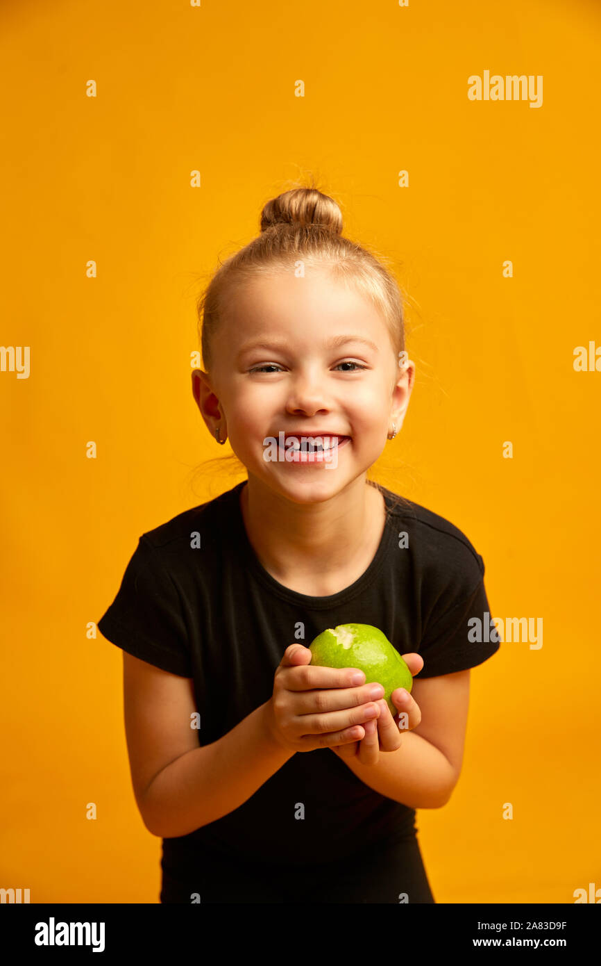 Little Ballerina ritratto su sfondo giallo, ritratto di un bambino felice sorridente e mostra il suo primo perso il dente di latte in mano una mela verde Foto Stock