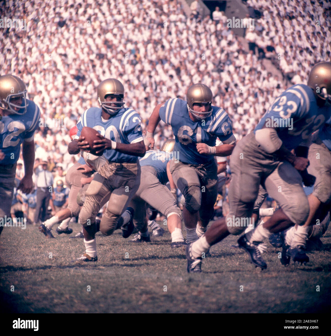 LOS ANGELES, CA - 6 ottobre: Singleton Ezell #20 del UCLA Bruins corre con la palla come il suo compagno di squadra Dave Stout #61 corre per blocco durante un gioco di NCAA contro la Ohio State Buckeyes il 6 ottobre 1962 presso il Los Angeles Memorial Coliseum di Los Angeles, California. (Foto di Hy Peskin) (numero impostato: X8760).Caption locale *** Ezell Singleton;Dave Stout Foto Stock