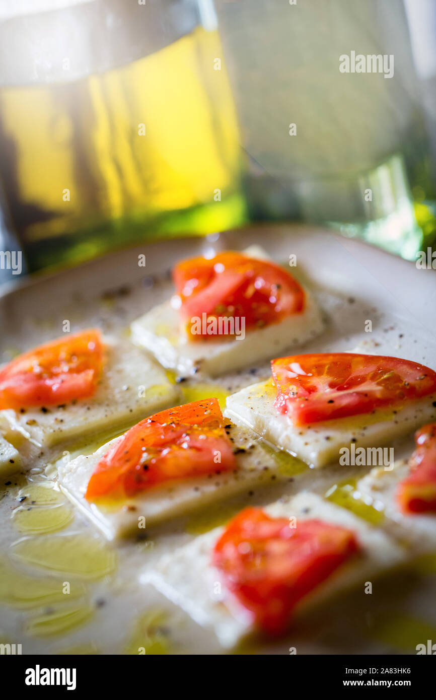 Le fette di pomodoro su piazze di mozzarella di bufala Formaggi spruzzata di olio nella luce solare Foto Stock